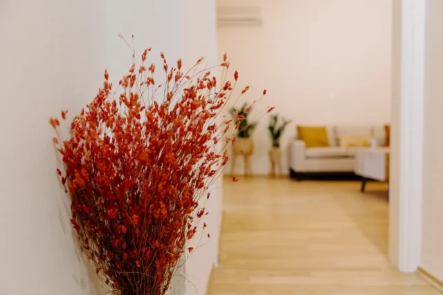 Ένα βάζο γεμάτο με έντονα κόκκινα λουλούδια στέκεται κομψά σε ένα διάδρομο, προσθέτοντας μια πινελιά χρώματος στον χώρο.